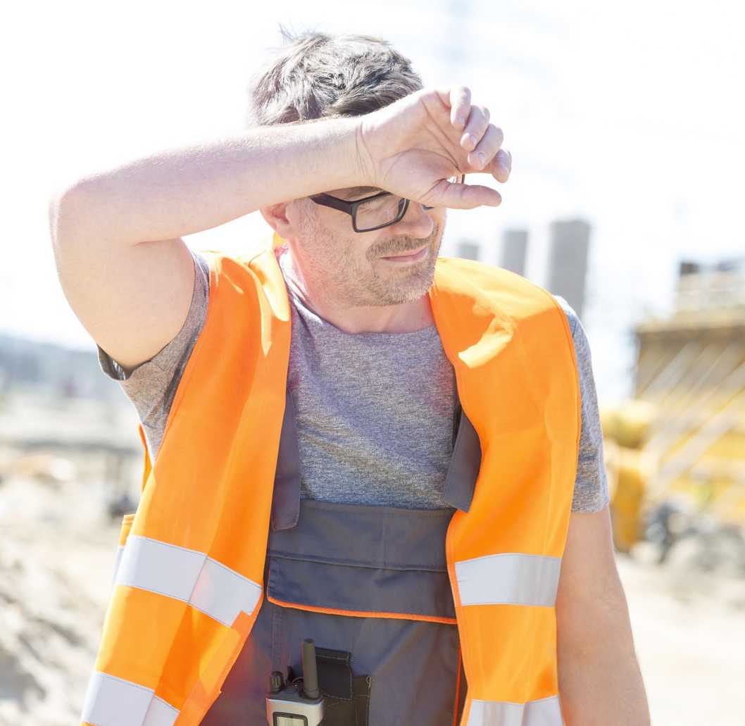 Photo of a worker wiping sweat off of his forehead while outside on a sunny day.